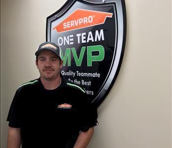 A man in a hat standing in front of SERVPRO sign. 