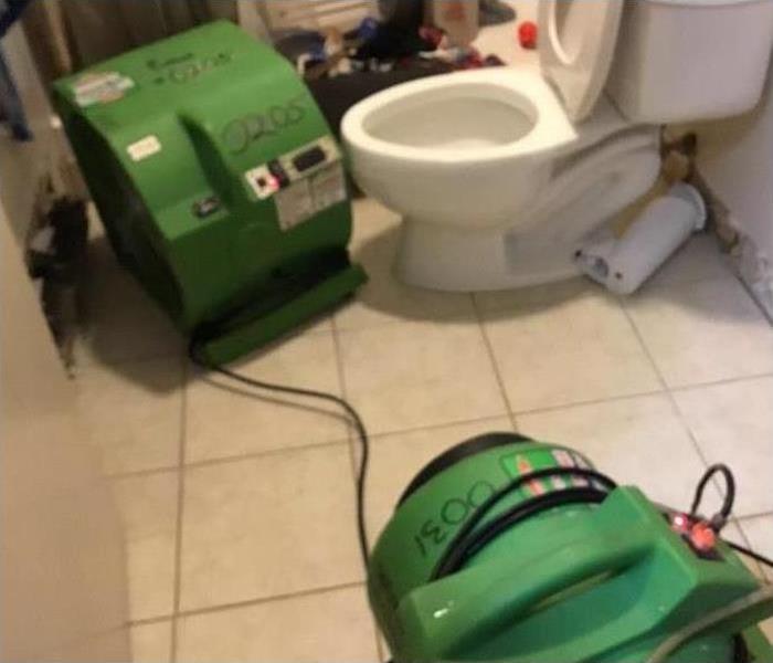 Restoration machines are cleaning water damage in a bathroom